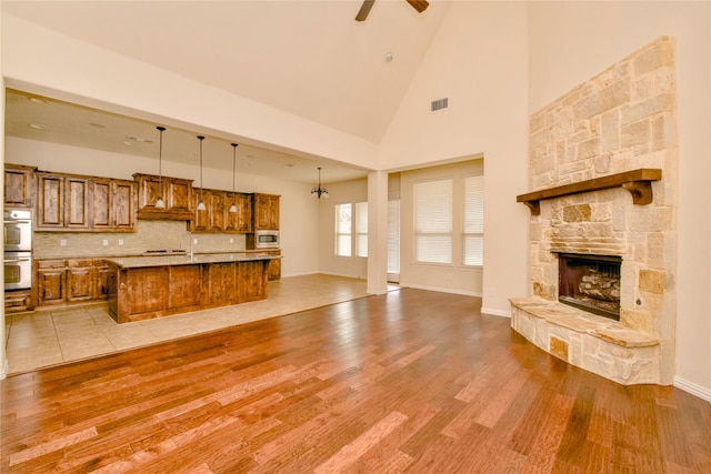 living room with ceiling fan, a stone fireplace, high vaulted ceiling, and light hardwood / wood-style flooring