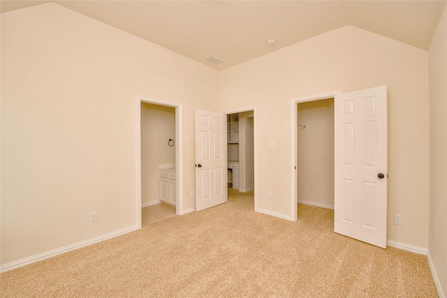 unfurnished bedroom with a walk in closet, light carpet, and vaulted ceiling