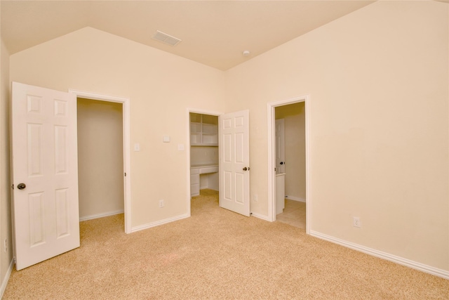 unfurnished bedroom with lofted ceiling, a walk in closet, light carpet, and a closet