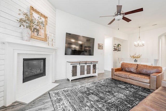 living room with a fireplace, ceiling fan with notable chandelier, and dark wood-type flooring