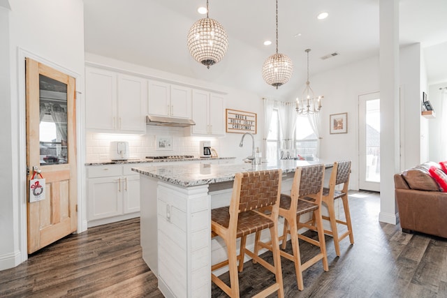 kitchen with dark hardwood / wood-style flooring, white cabinetry, a kitchen island with sink, and hanging light fixtures