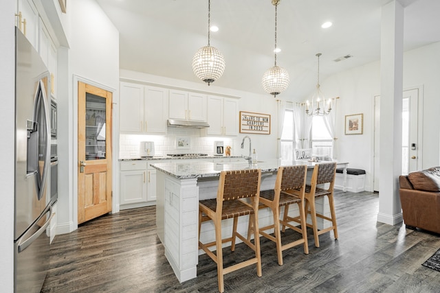 kitchen featuring pendant lighting, stainless steel appliances, an island with sink, and white cabinets