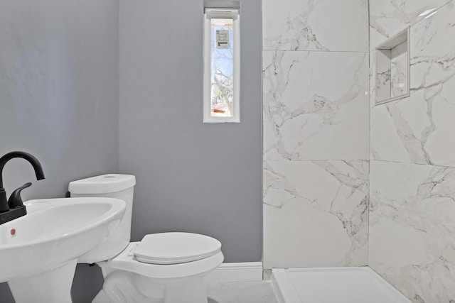 bathroom featuring a tile shower, toilet, and sink