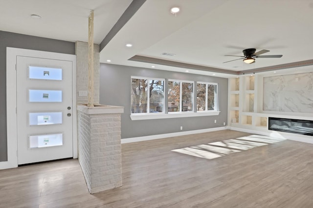 unfurnished living room featuring a tray ceiling, ceiling fan, and light hardwood / wood-style floors