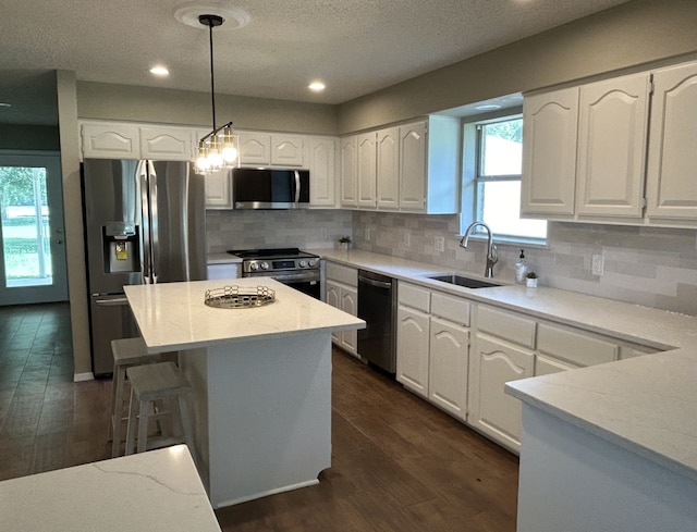 kitchen featuring stainless steel appliances, white cabinetry, sink, and decorative light fixtures