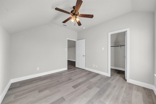 unfurnished bedroom featuring lofted ceiling, ceiling fan, a spacious closet, light hardwood / wood-style floors, and a closet