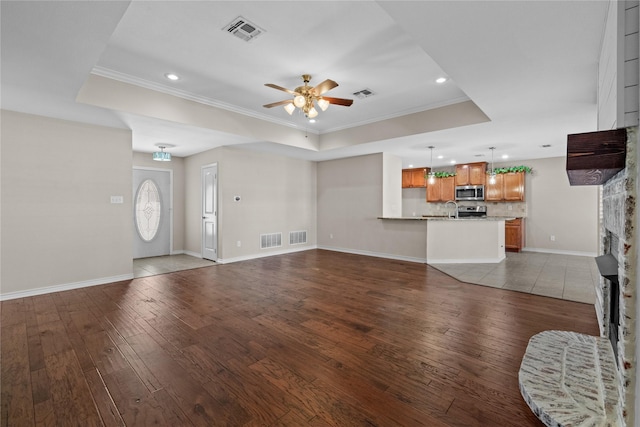 unfurnished living room with a fireplace, hardwood / wood-style flooring, ornamental molding, ceiling fan, and a raised ceiling