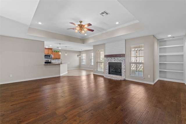 unfurnished living room with a brick fireplace, ornamental molding, ceiling fan, dark wood-type flooring, and built in features