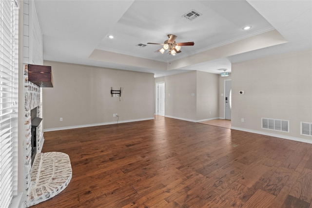 unfurnished living room with ceiling fan, dark wood-type flooring, a brick fireplace, a raised ceiling, and crown molding