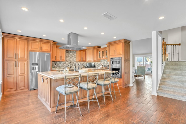 kitchen with a spacious island, a kitchen bar, island range hood, stainless steel appliances, and light stone countertops