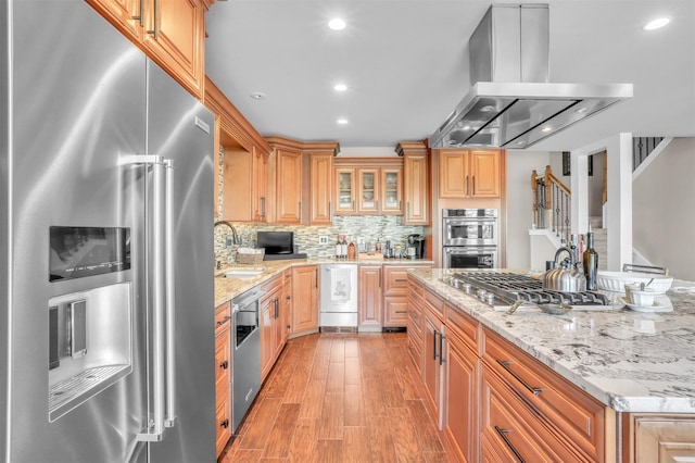 kitchen featuring sink, island range hood, light hardwood / wood-style flooring, stainless steel appliances, and light stone countertops