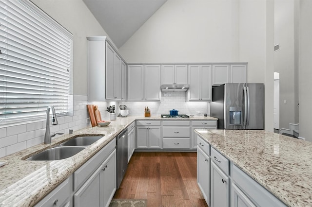 kitchen with light stone countertops, appliances with stainless steel finishes, sink, high vaulted ceiling, and white cabinetry