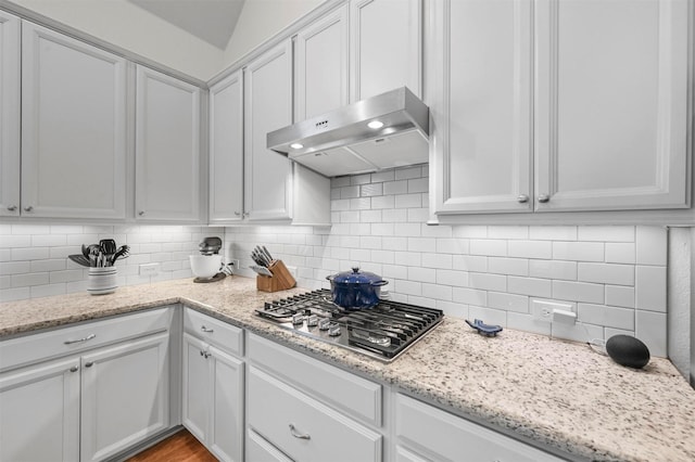 kitchen featuring stainless steel gas stovetop, backsplash, light stone countertops, range hood, and white cabinetry