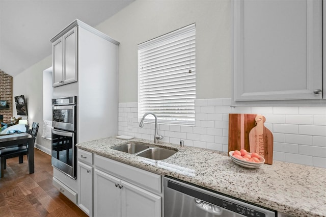 kitchen featuring appliances with stainless steel finishes, dark hardwood / wood-style flooring, backsplash, light stone counters, and sink