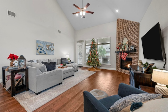 living room featuring hardwood / wood-style flooring, ceiling fan, high vaulted ceiling, and a brick fireplace