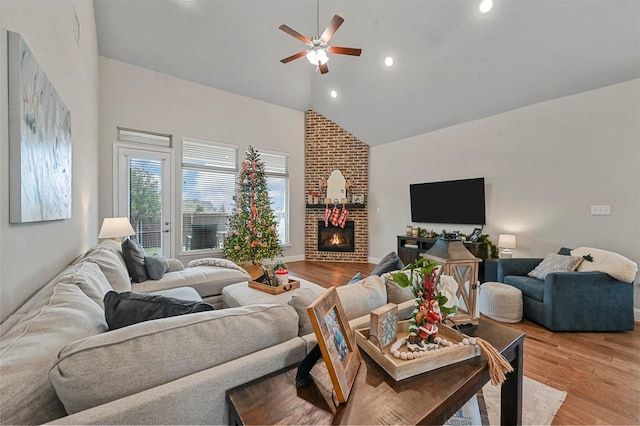 living room featuring high vaulted ceiling, light hardwood / wood-style floors, a brick fireplace, and ceiling fan