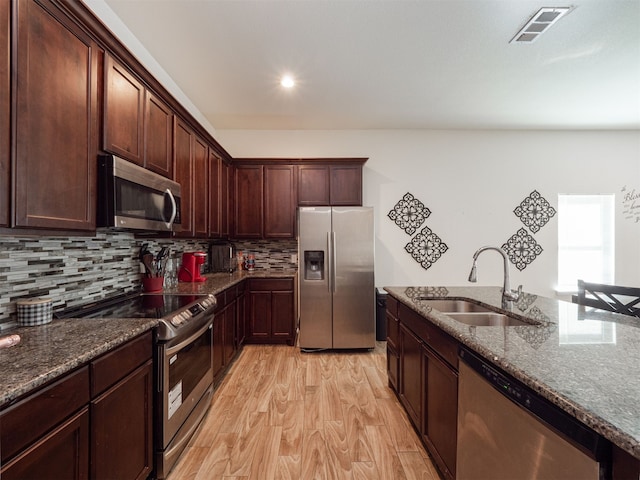 kitchen with sink, tasteful backsplash, dark stone countertops, appliances with stainless steel finishes, and light wood-type flooring