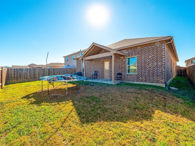 back of house with a trampoline, a patio area, and a lawn