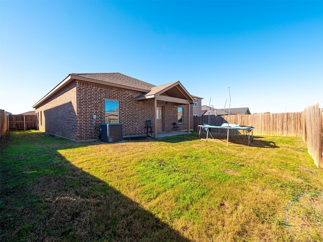 rear view of property with a trampoline, a lawn, a patio area, and central air condition unit