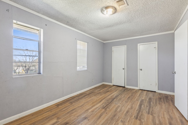 unfurnished bedroom featuring visible vents, ornamental molding, a textured ceiling, wood finished floors, and baseboards