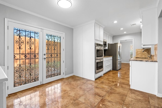 kitchen with appliances with stainless steel finishes, ornamental molding, sink, dark stone countertops, and white cabinetry