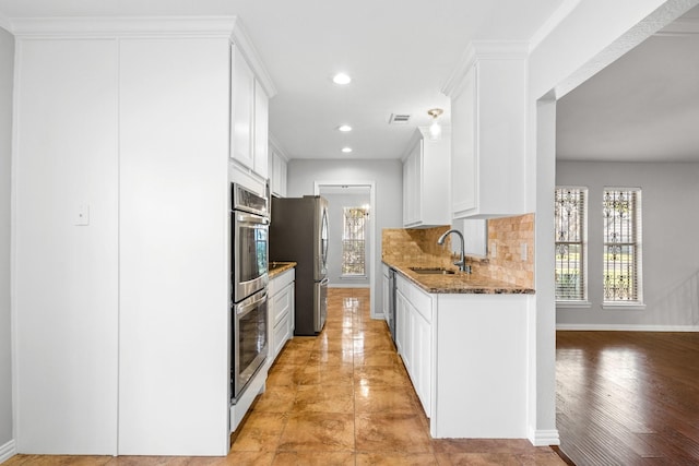 kitchen featuring dark stone counters, sink, appliances with stainless steel finishes, light hardwood / wood-style floors, and white cabinetry