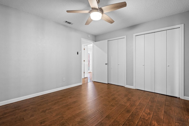 unfurnished bedroom featuring a textured ceiling, ceiling fan, dark hardwood / wood-style flooring, and two closets