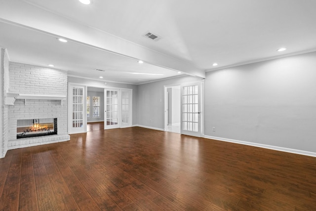 unfurnished living room with a brick fireplace, wood-type flooring, ornamental molding, and french doors