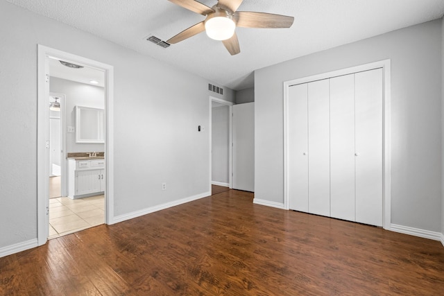 unfurnished bedroom with ceiling fan, a textured ceiling, connected bathroom, wood-type flooring, and a closet