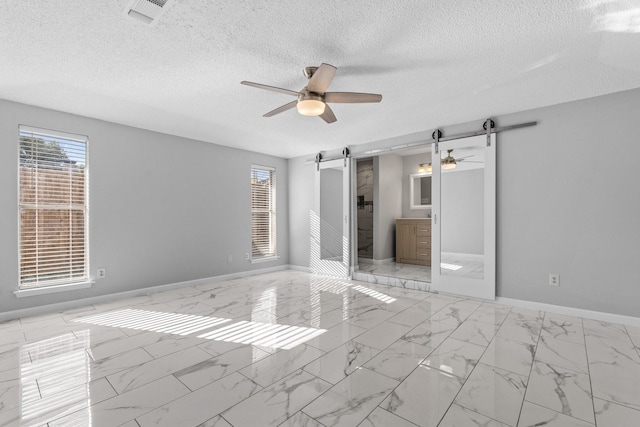 empty room featuring ceiling fan, a barn door, and a textured ceiling