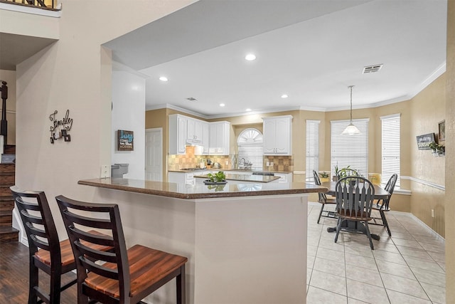 kitchen with light tile patterned floors, kitchen peninsula, pendant lighting, a kitchen bar, and white cabinets