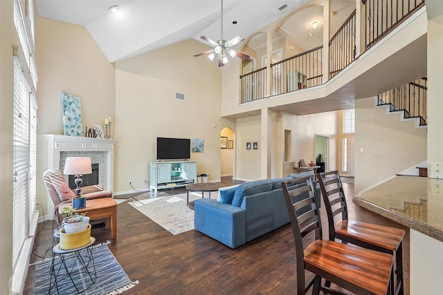 living room featuring a high ceiling, dark hardwood / wood-style floors, ceiling fan, and a tiled fireplace