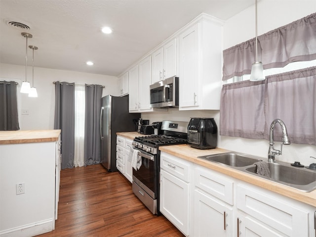 kitchen with pendant lighting, butcher block counters, sink, white cabinetry, and stainless steel appliances