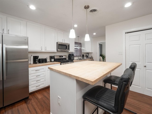 kitchen with butcher block countertops, a kitchen breakfast bar, white cabinetry, and stainless steel appliances