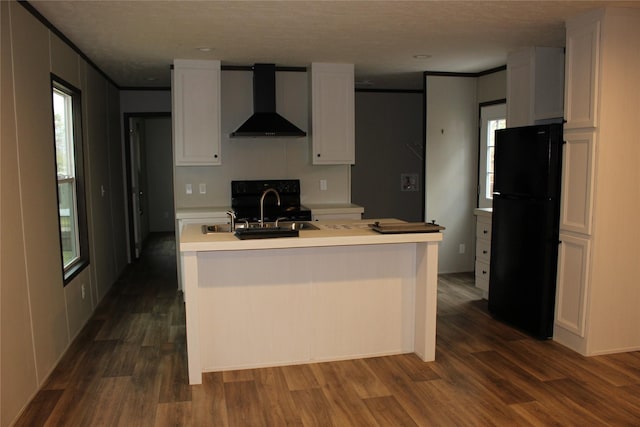 kitchen with dark wood-type flooring, black refrigerator, sink, wall chimney exhaust hood, and white cabinetry