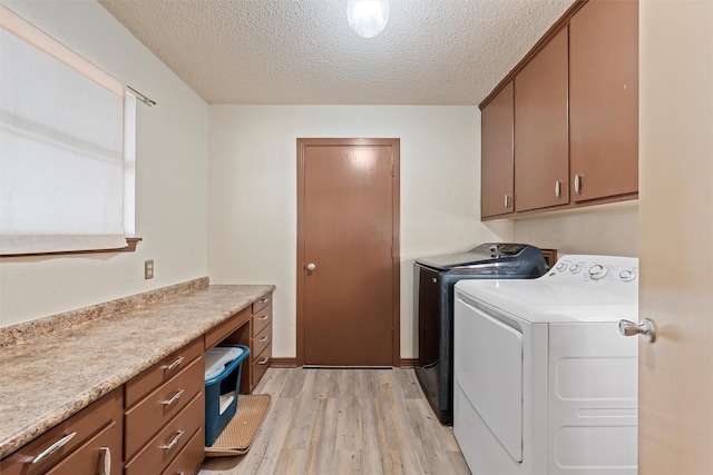 clothes washing area featuring washing machine and clothes dryer, cabinets, a textured ceiling, and light wood-type flooring