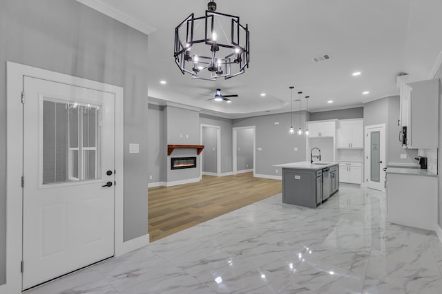 kitchen featuring pendant lighting, a kitchen island with sink, ceiling fan with notable chandelier, sink, and white cabinetry