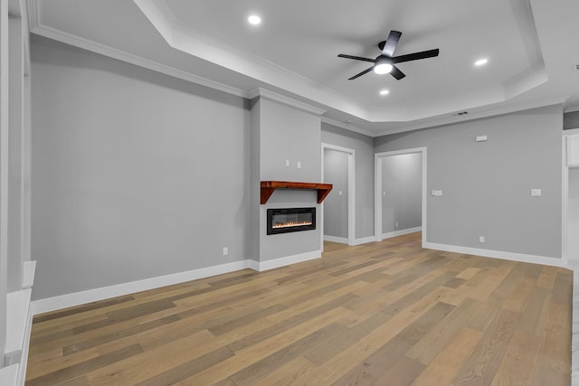 unfurnished living room with a tray ceiling, crown molding, ceiling fan, and light hardwood / wood-style floors