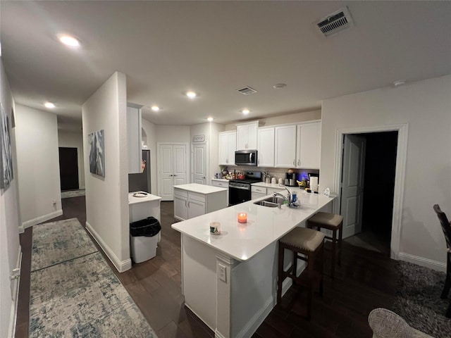 kitchen with white cabinetry, sink, stainless steel appliances, a kitchen breakfast bar, and kitchen peninsula