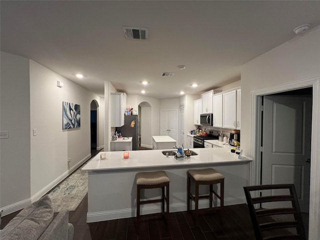 kitchen featuring dark wood-type flooring, kitchen peninsula, a kitchen bar, white cabinets, and appliances with stainless steel finishes