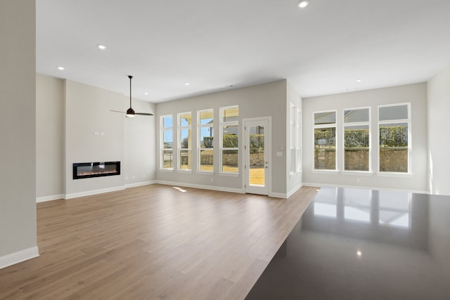 unfurnished living room featuring baseboards, a glass covered fireplace, ceiling fan, light wood-style floors, and recessed lighting