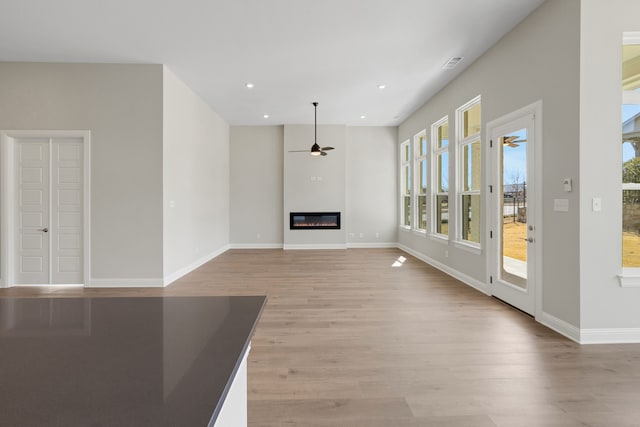 unfurnished living room featuring a glass covered fireplace, baseboards, ceiling fan, and light wood finished floors