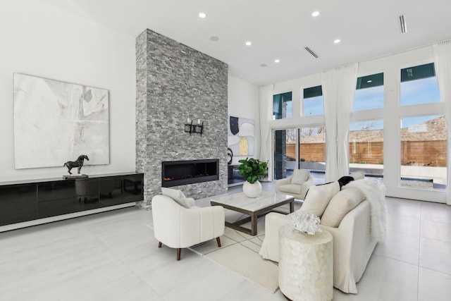 tiled living room featuring a towering ceiling, a stone fireplace, and a healthy amount of sunlight