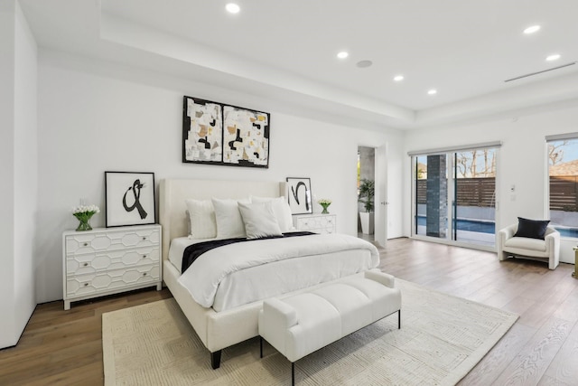 bedroom with access to exterior, wood-type flooring, and a tray ceiling