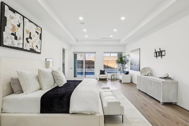 bedroom with light hardwood / wood-style floors, a tray ceiling, and access to outside