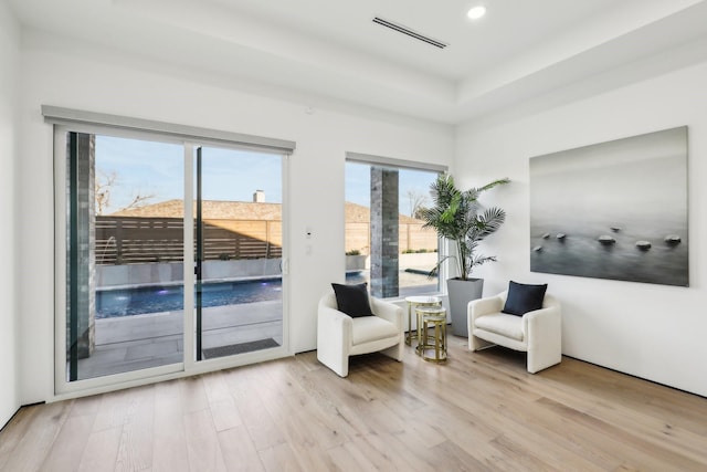 living area featuring plenty of natural light, a tray ceiling, and light wood-type flooring