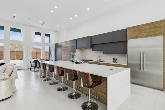 kitchen with appliances with stainless steel finishes, a towering ceiling, sink, a breakfast bar, and a center island with sink