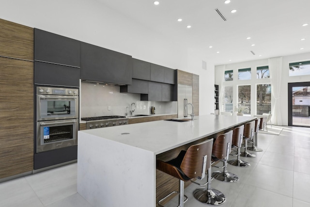 kitchen featuring appliances with stainless steel finishes, a kitchen bar, a large island with sink, and sink