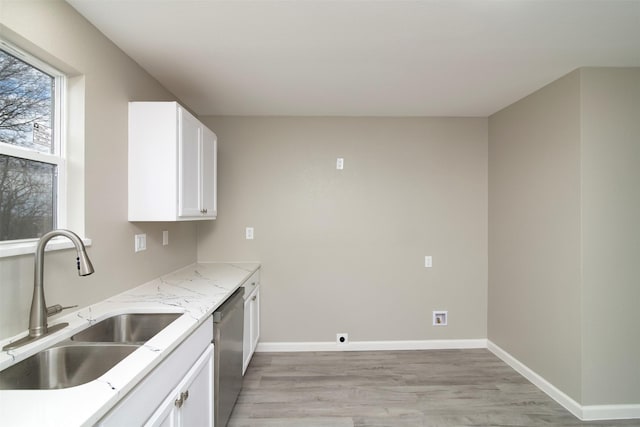 kitchen with sink, light stone counters, stainless steel dishwasher, light hardwood / wood-style floors, and white cabinets