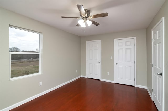 unfurnished bedroom with dark hardwood / wood-style floors, ceiling fan, and multiple closets